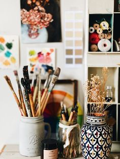 an assortment of art supplies sitting on top of a wooden table next to a vase