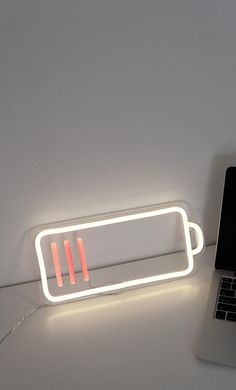 a laptop computer sitting on top of a white desk next to a neon light sign