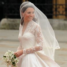 the bride is walking down the street in her wedding dress and veil with flowers on it