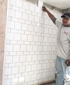 a man standing in front of a white brick wall holding a hammer and pointing at something