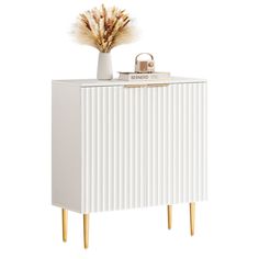 a white cabinet with wooden legs and a vase filled with dry grass on top of it