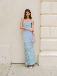 a woman standing in front of a white wall wearing a blue dress with flowers on it