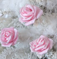 three pink roses sitting on top of white feathers in the shape of snowflakes