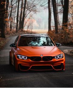 an orange car parked on the side of a road in front of some tall trees