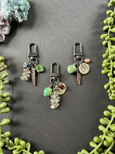 three charms are sitting on a table next to some green beads and corals in the background