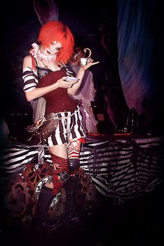 a woman with red hair is dressed up as a clown and holding a cat in her hand