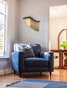 a blue chair sitting in front of a window next to a table with a mirror on it