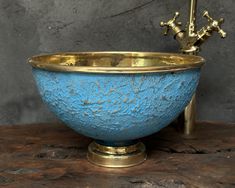 a blue and gold bowl sitting on top of a wooden table next to a faucet