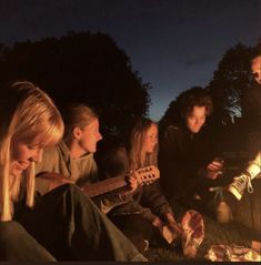 a group of young people sitting around a campfire playing guitars and singing to the music