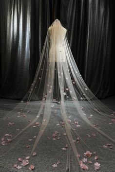 a wedding veil with pink flowers on the floor in front of a black curtained backdrop