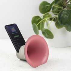 a pink speaker sitting on top of a table next to a cell phone and potted plant