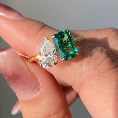 a woman's hand holding an emerald and diamond ring