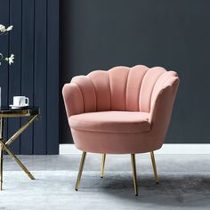 a pink chair sitting next to a table with a vase on it and flowers in the background