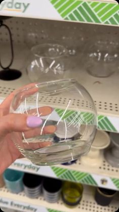 a person holding a clear glass in front of a shelf filled with bottles and glasses