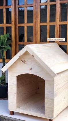 a dog house made out of plywood is sitting in front of a door with potted plants