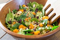 a wooden bowl filled with spinach, carrots and other vegetables