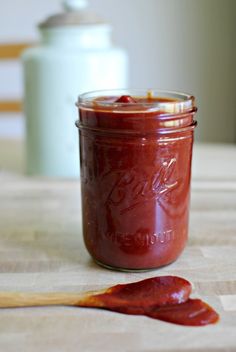 a jar filled with ketchup sitting on top of a table next to a wooden spoon