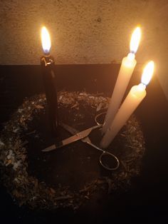 three lit candles sitting on top of a table next to a pair of scissor