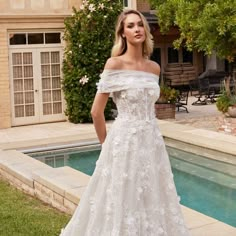 a woman standing in front of a pool wearing a wedding dress with flowers on it