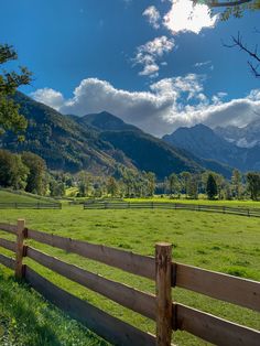 a wooden fence in the middle of a grassy field with mountains in the back ground