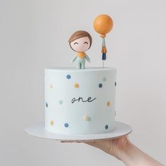 a person holding up a cake with two people on top and one balloon in the air