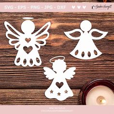 three angel cutouts on top of a wooden table next to a candle and some candles