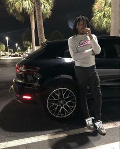 a person standing next to a car talking on a cell phone with palm trees in the background