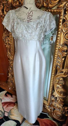 "This gown is a stunner!  From the 60's.  Made of silver silk shantung.  The top of the dress is heavily beaded in silver and clear glass beads, sequins and auraborealice prong set rhinestones.  Empire waist.  Center back zip.  No holes or stains.  There are a couple of loose beads but all are there.  Best fit would be a Large, however, please see the measurements below for a proper fit.  All sales are final. Measurements Armpit-armpit doubled 40\" Waist 34\" Hip 44\"" Silver Sparkling Evening Dress With Fitted Bodice, Glamorous Fitted Satin Mother Of The Bride Dress, Elegant Silver Dress With Pearl Embroidery, Vintage Silver Dress For Formal Occasions, Silver Vintage Dress For Formal Occasions, Evening Dress With Pearl Embroidery And Fitted Bodice, Silver Vintage Dresses For Formal Occasions, Silver Vintage Formal Dresses, Silver Silk Evening Dress For Gala