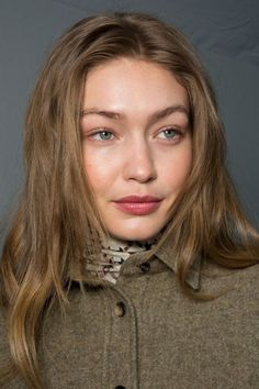 a woman with long blonde hair and blue eyes wearing a green coat, looking at the camera