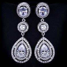 A delightfully unique pair of bridal earrings with an incredible sparkle! Adorned with flawlessly faceted cubic zirconia that capture the light in a dazzling array of sparkles, the earrings are rhodium plated for a bright finish which enhances the intricate detailing and conveys a modern take on old elegance. Overall length of the earring is 52mm (approx. 2"). Hypoallergenic - lead, nickel and cadmium free. This exquisite design will add a touch of sophistication to any wedding gown or formal en Dazzling Halo Design Bridal Earrings For Party, Halo Design Cubic Zirconia Bridal Drop Earrings, Bridal Halo Design Cubic Zirconia Drop Earrings, Party Bridal Earrings With Halo Design And Cubic Zirconia, Silver Brilliant Cut Teardrop Earrings For Wedding, Cubic Zirconia Bridal Earrings, Blue Earrings Wedding, Winter Bridal Jewelry, Long Bridal Earrings