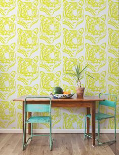 two green chairs sitting at a wooden table in front of a wall with yellow and white designs on it