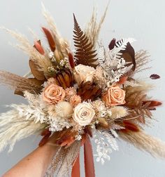 a bouquet of dried flowers and feathers in someone's hand