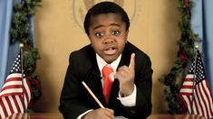 a young boy in a suit and tie making a peace sign with two american flags behind him