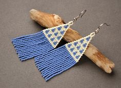 two pairs of blue and white knitted earrings hanging from wooden hooks on a gray surface