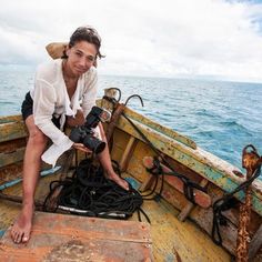 a man sitting on top of a wooden boat in the middle of the ocean holding a camera