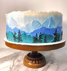 a cake with blue frosting and trees on it sitting on a marble counter top