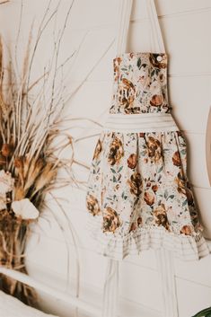 a flowered dress hanging on the wall next to a potted plant and mirror