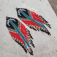 two red, black and blue beaded earrings sitting on top of a cement slab