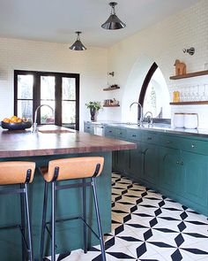 a kitchen with green cabinets and black and white tile flooring, two bar stools in front of the island