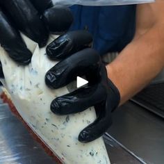 a person wearing black gloves holding a piece of cheese