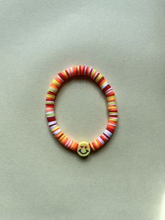 Orange, yellow, red and white clay bracelet with a smiley face charm. Fits most wrist sizes. Red Smiley Face Clay Bracelet, Adjustable Smiley Face Round Bead Bracelets, Playful Multicolor Beaded Bracelets With Smiley Face, Playful Multicolor Smiley Face Beaded Bracelets, Clay Bracelet, White Clay, Smiley Face, Orange Yellow, Smiley