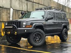 a black jeep is parked in front of a concrete wall on a rainy day with yellow lines