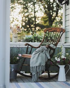 an old rocking chair with a blanket on it and some flowers in the vases