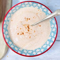 a bowl of food with a spoon in it on a blue and red plate next to a cutting board