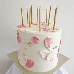 a white cake with pink frosting and gold candles sitting on top of a table