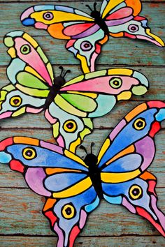 three colorful butterflies sitting on top of a wooden table