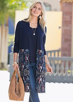 a woman is walking down the street carrying a purse and wearing a blue cardigan