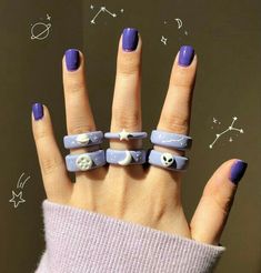 a woman's hand with purple and white nail polish holding five rings that have skulls on them