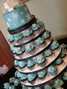 a multi layer cake with frosting and cupcakes on it sitting on top of a table