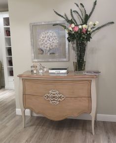 a vase with flowers sitting on top of a wooden dresser